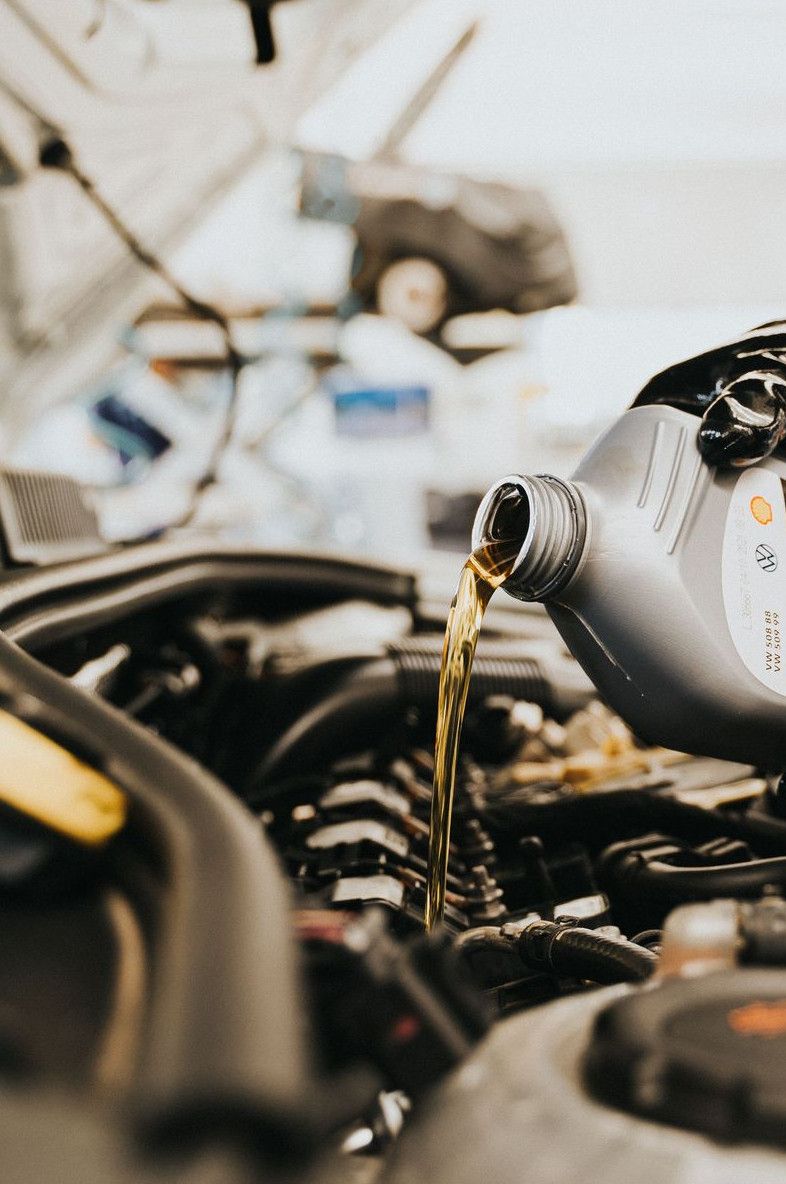 Close-up of a mechanic pouring engine oil into a car engine in an auto repair shop.